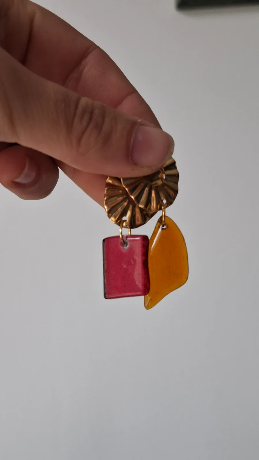Boucles d'oreilles en verre translucide rose et orange tenues à contre-jour devant un paysage.