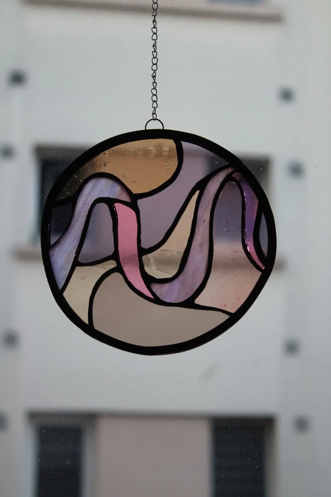Vitrail circulaire posé à plat, révélant des reflets irisés et des verres aux teintes violacées.