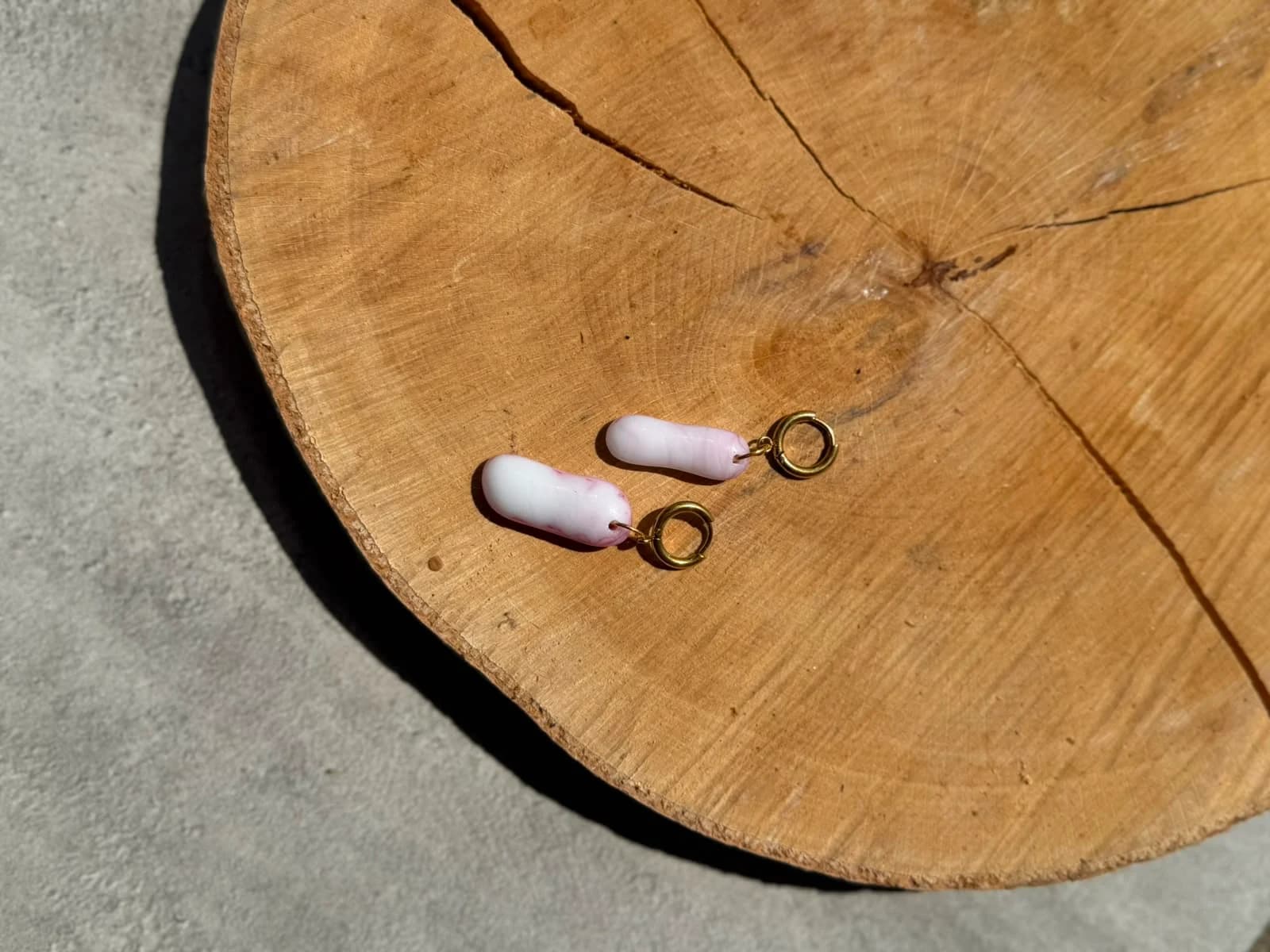 Main tenant les deux pendentifs arrondis en verre rose et blanc montés sur anneaux dorés.