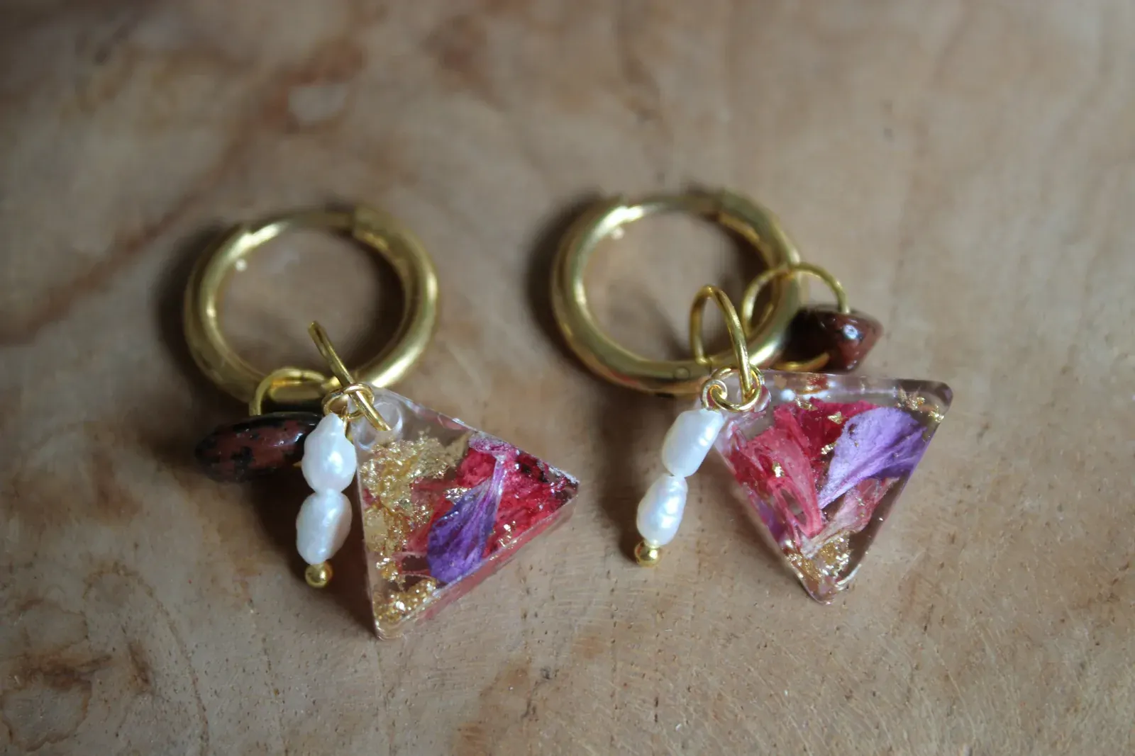 Gros plan sur une boucle d'oreille dorée avec inclusion de pétales roses, feuille d'or et perle d'eau douce