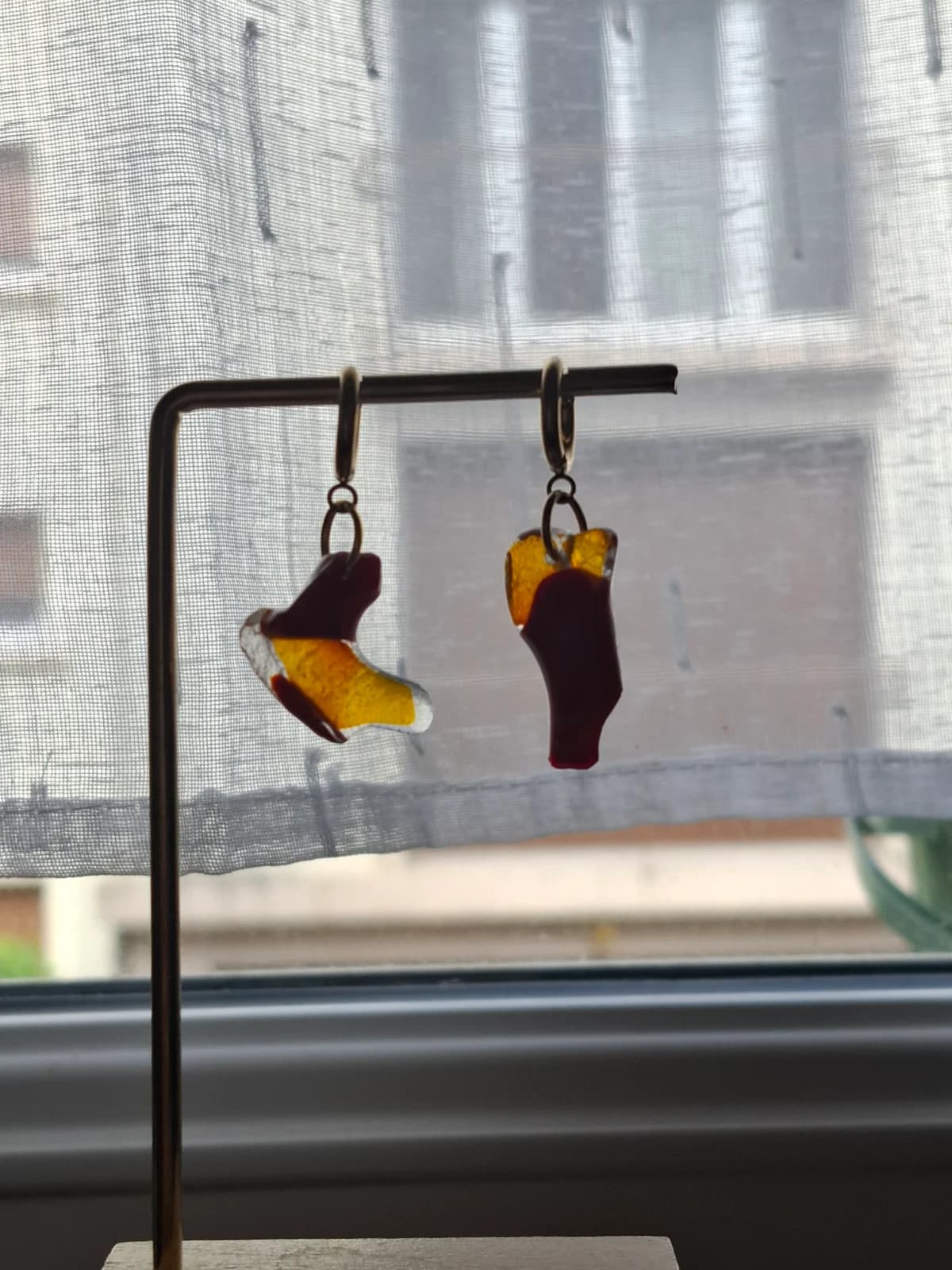 Boucles d'oreilles en verre rouge et jaune suspendues à un présentoir doré devant une plante verte.