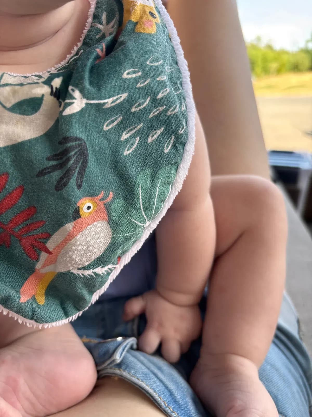 Bébé portant le bavoir bandana vert à motifs d'oiseau et de végétation colorée.