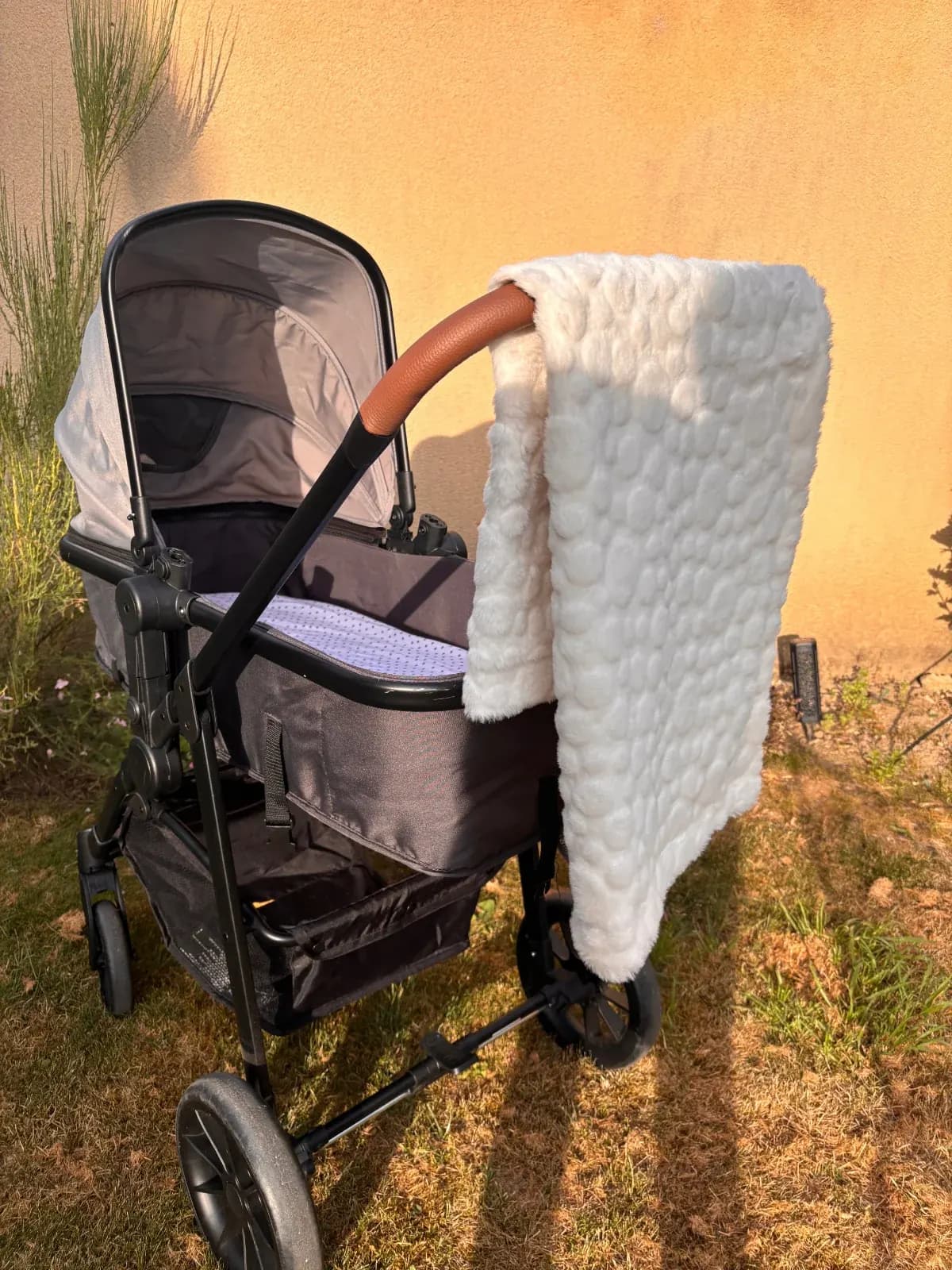 Polaire blanche texturée de la couverture pour bébé, posée sur la poignée d'une poussette.