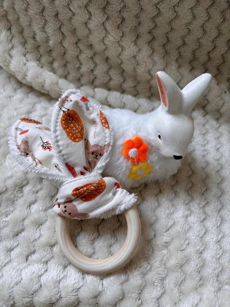 Anneau de dentition en bois et tissu aux tons chauds présenté à côté d'une figurine de lapin blanc.