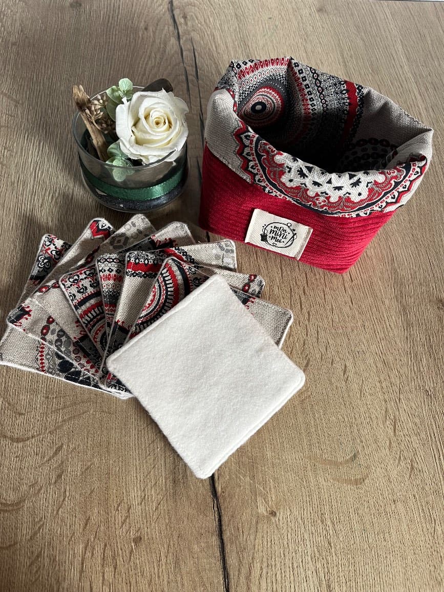 Panier en tissu côtelé rouge garni de ses lingettes carrées coordonnées, posé sur une table.