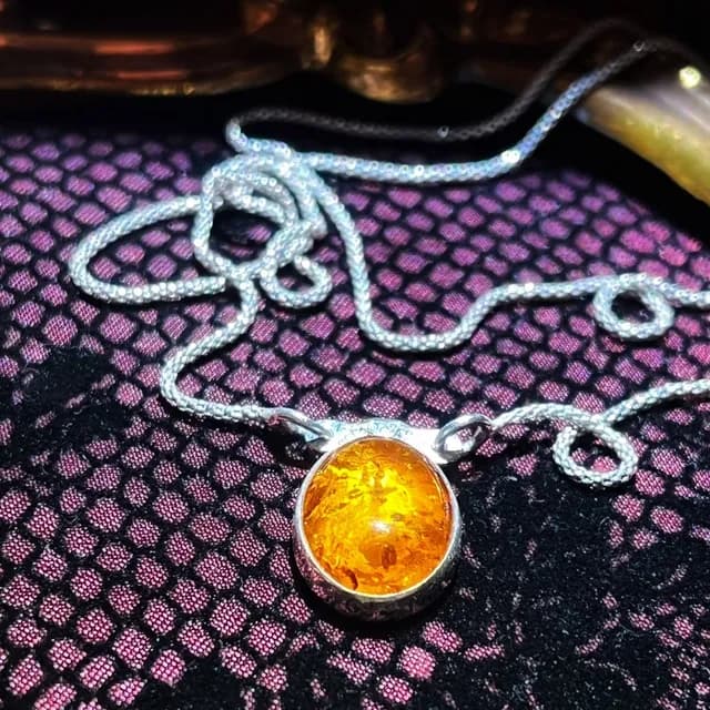 Gros plan sur le pendentif ovale en ambre jaune doré serti d'argent et sa chaîne argentée en maille travaillée
