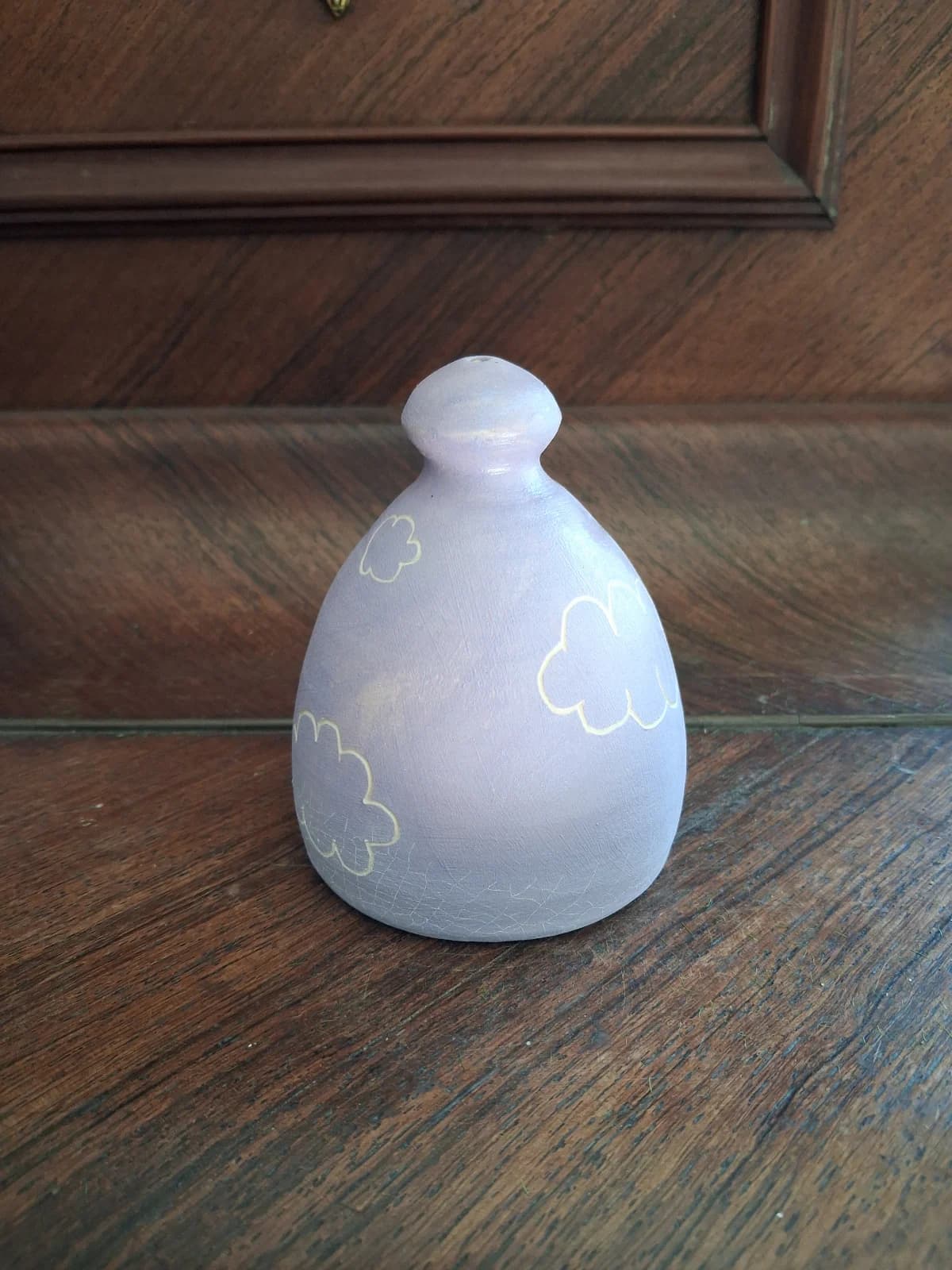 Arrosoir-main bombé en céramique mauve clair à motifs de nuages blancs posé sur du bois