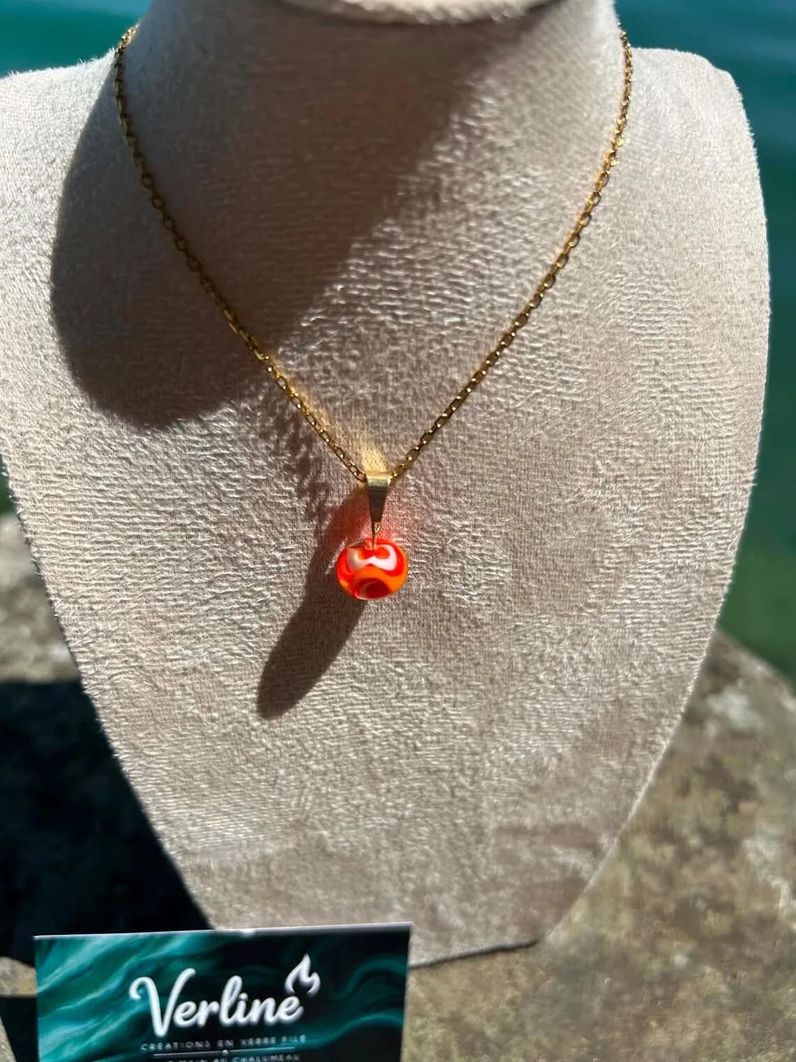 Vue rapprochée du pendentif en verre filé aux nuances orange et blanches sur chaîne dorée.