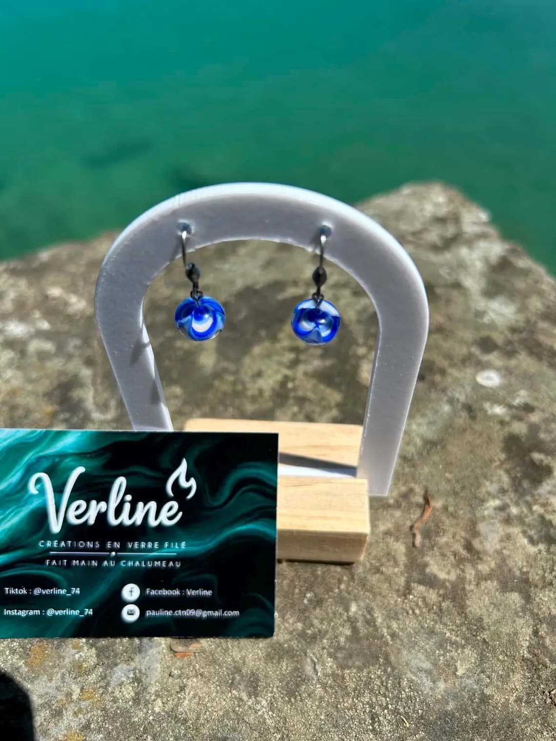 Vue plongeante des boucles d’oreilles en perles de verre bleu et blanc sur présentoir devant l'eau