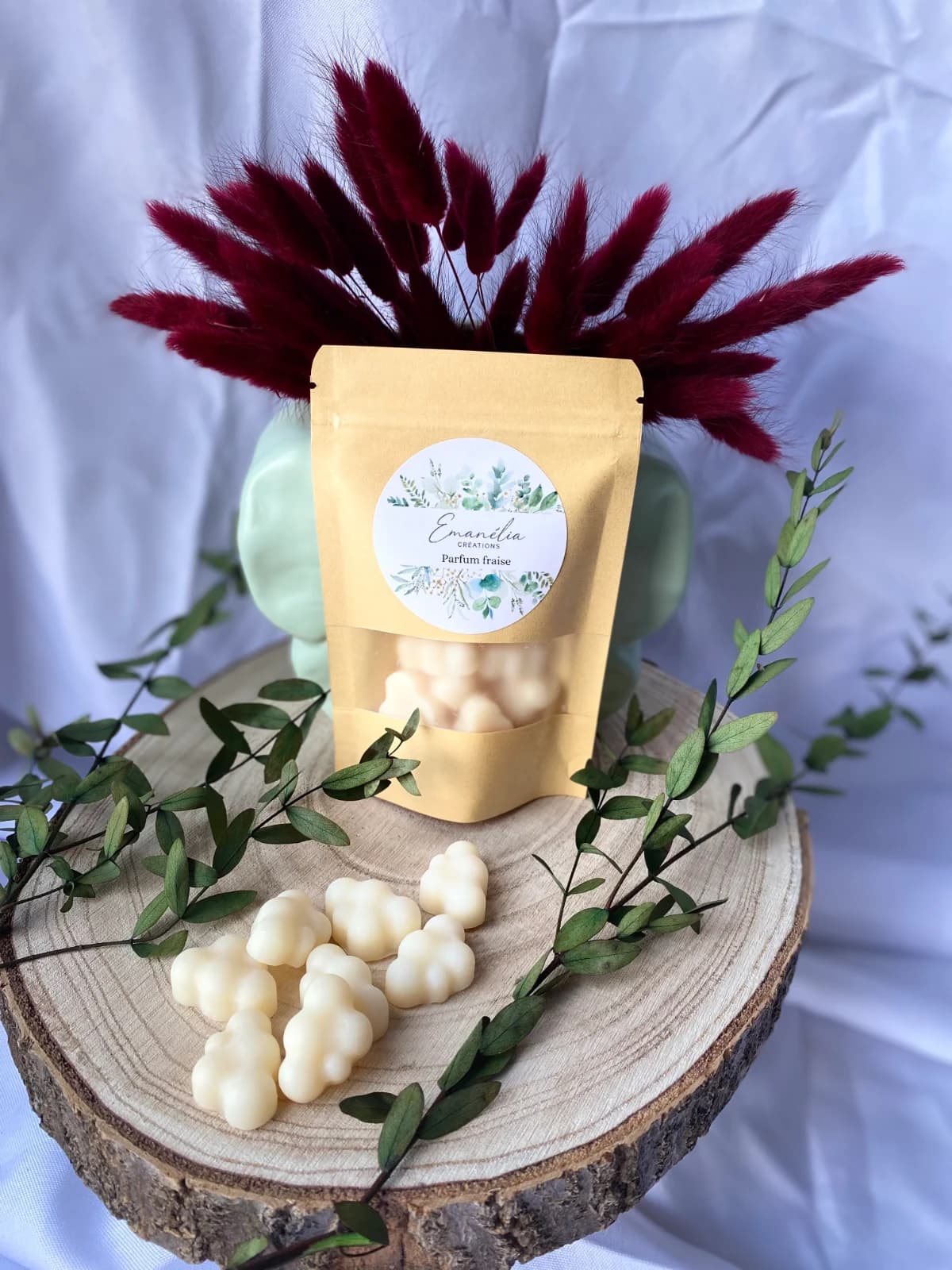 Sachet kraft et fondants parfumés en forme de nuages disposés sur un rondin de bois décoré de feuillage.